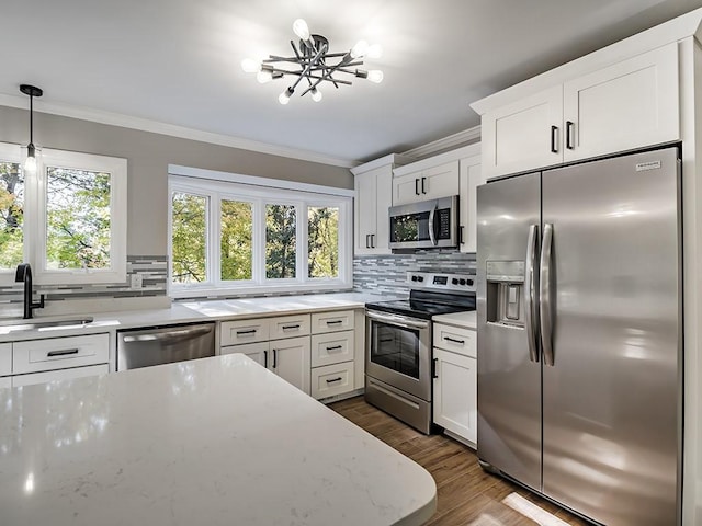 kitchen featuring pendant lighting, sink, crown molding, appliances with stainless steel finishes, and white cabinets