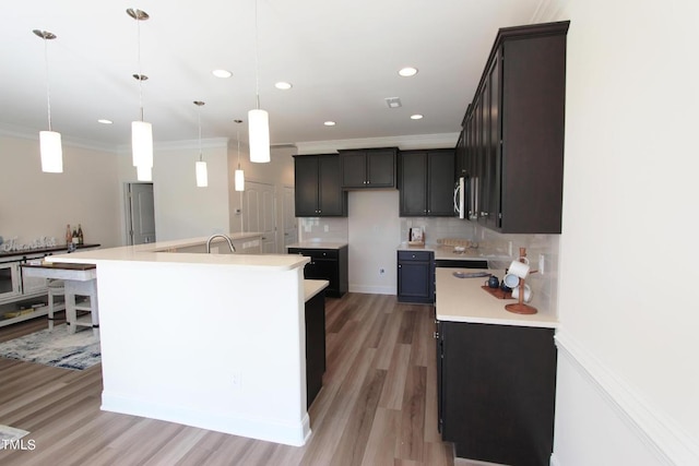 kitchen with crown molding, a kitchen island with sink, decorative backsplash, and decorative light fixtures