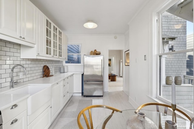 kitchen with sink, white cabinetry, crown molding, stainless steel refrigerator, and decorative backsplash