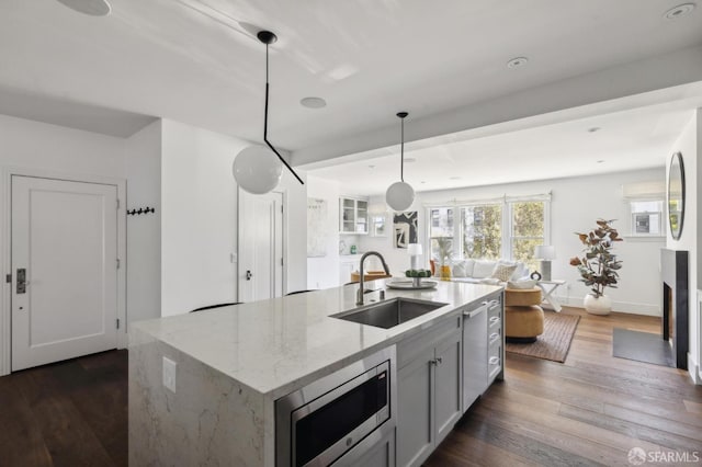 kitchen featuring sink, dark hardwood / wood-style floors, stainless steel microwave, light stone counters, and decorative light fixtures