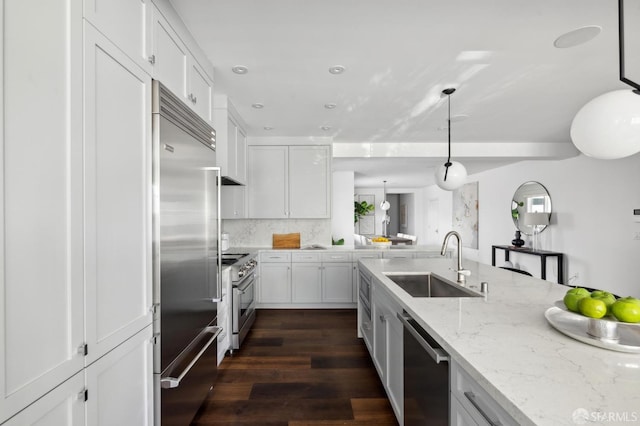 kitchen with decorative light fixtures, high quality appliances, sink, white cabinets, and backsplash