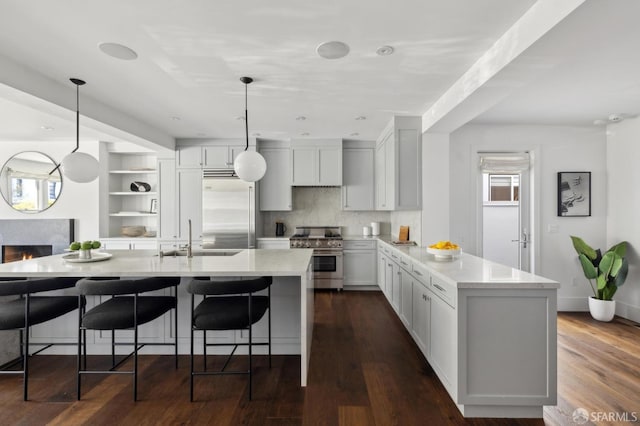 kitchen featuring pendant lighting, sink, a kitchen island with sink, high end appliances, and decorative backsplash