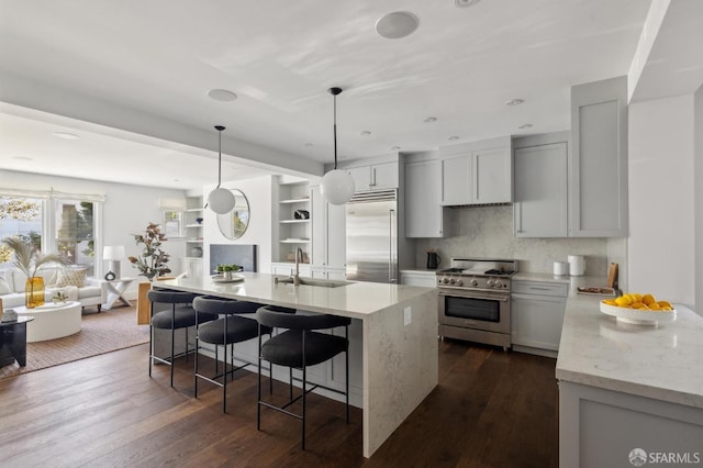 kitchen with pendant lighting, an island with sink, sink, high end appliances, and light stone counters