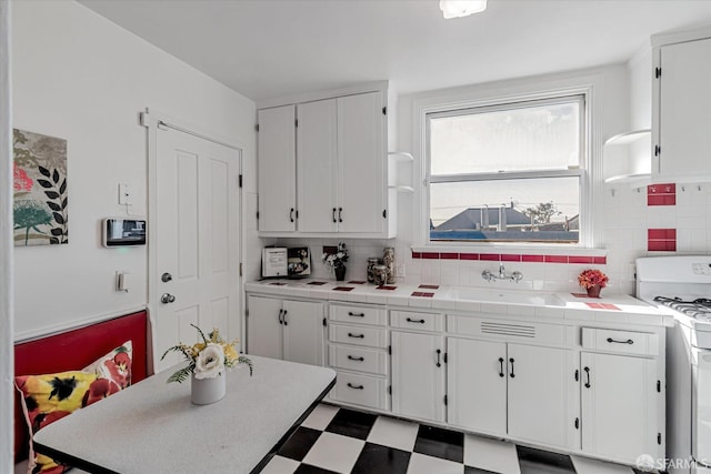 kitchen featuring a sink, backsplash, white range with gas stovetop, and white cabinets