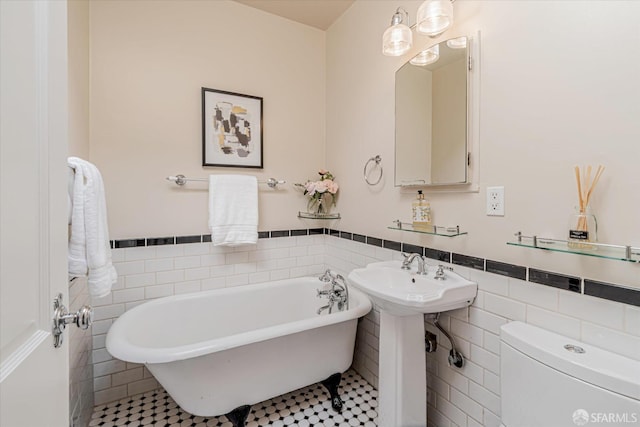 bathroom with a wainscoted wall, toilet, a freestanding tub, tile walls, and a sink