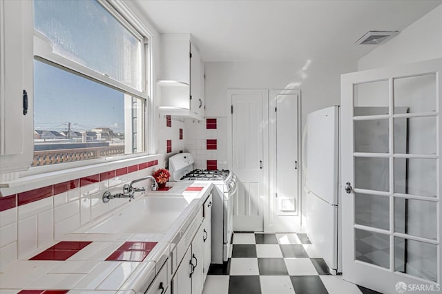 kitchen featuring a wealth of natural light, tile patterned floors, a sink, white appliances, and tile counters