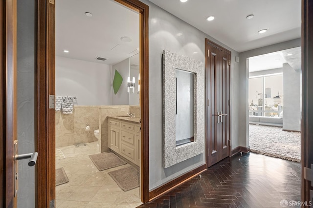 bathroom with toilet, vanity, parquet flooring, and tile walls