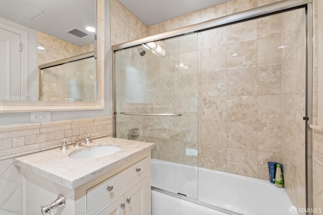 bathroom with tile walls, vanity, and combined bath / shower with glass door