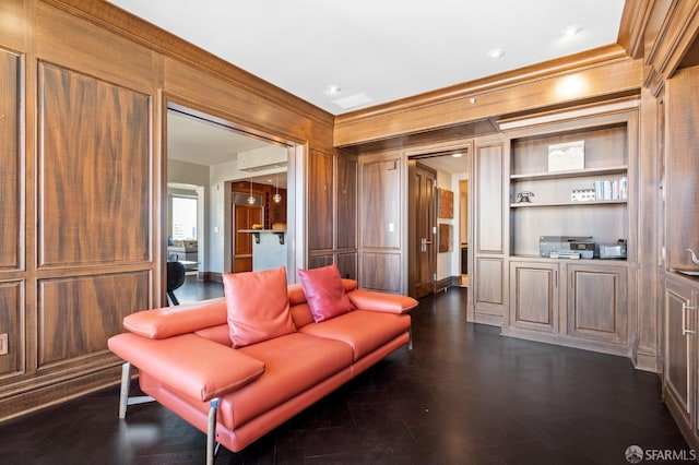 living room with built in shelves, dark wood-type flooring, wooden walls, and crown molding