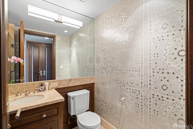 bathroom with toilet, vanity, and tile walls