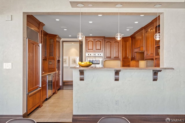 kitchen featuring stainless steel oven, decorative light fixtures, paneled built in fridge, a breakfast bar area, and kitchen peninsula