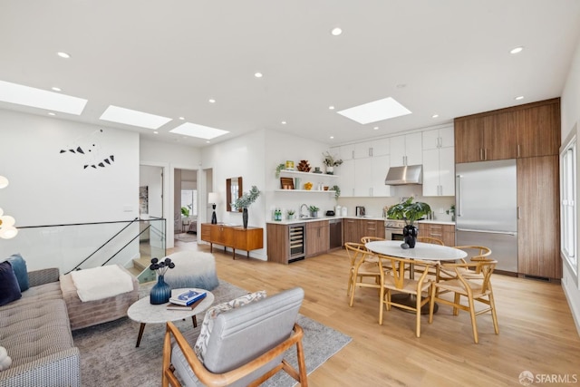 living room featuring a skylight, light wood-style flooring, wine cooler, and recessed lighting