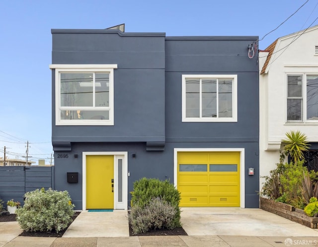 view of front of property featuring a garage, concrete driveway, fence, and stucco siding