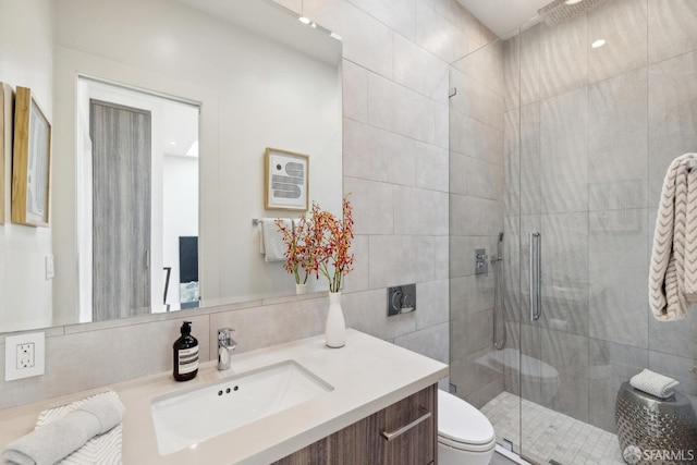 bathroom featuring toilet, a tile shower, tile walls, and vanity