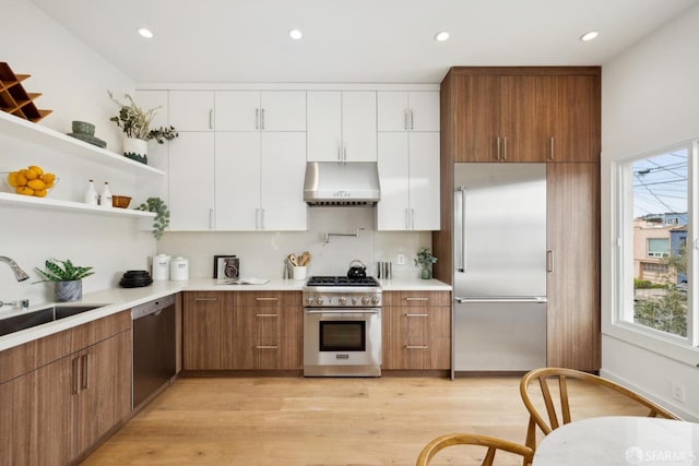 kitchen with high end appliances, brown cabinetry, white cabinets, a sink, and under cabinet range hood