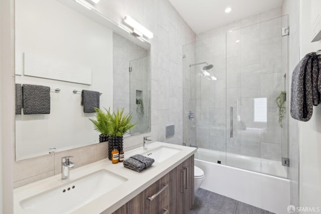 full bathroom with toilet, shower / bath combination with glass door, double vanity, and a sink