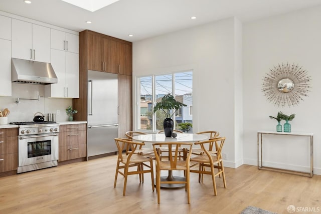 kitchen with high end appliances, light countertops, light wood-type flooring, under cabinet range hood, and white cabinetry