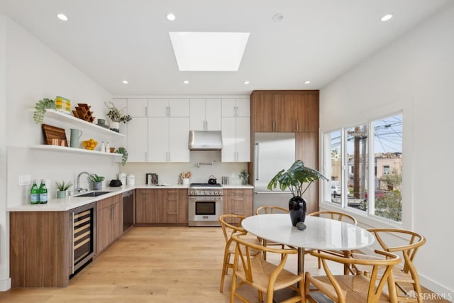 kitchen with a skylight, wine cooler, high end appliances, a sink, and under cabinet range hood