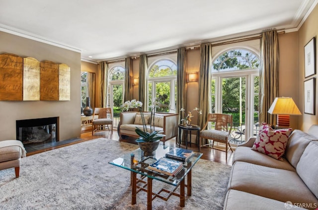 living room with a wealth of natural light, ornamental molding, a fireplace with flush hearth, and wood finished floors