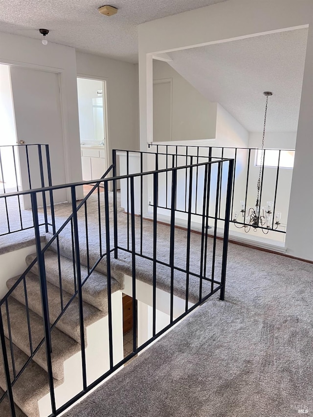 stairs featuring carpet flooring, a notable chandelier, lofted ceiling, and a textured ceiling