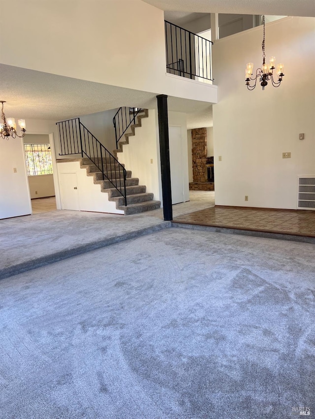 unfurnished living room with a stone fireplace, a towering ceiling, carpet floors, and a chandelier