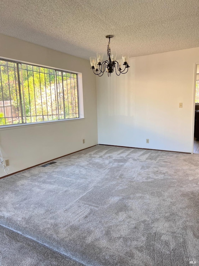 carpeted empty room featuring a notable chandelier and a textured ceiling