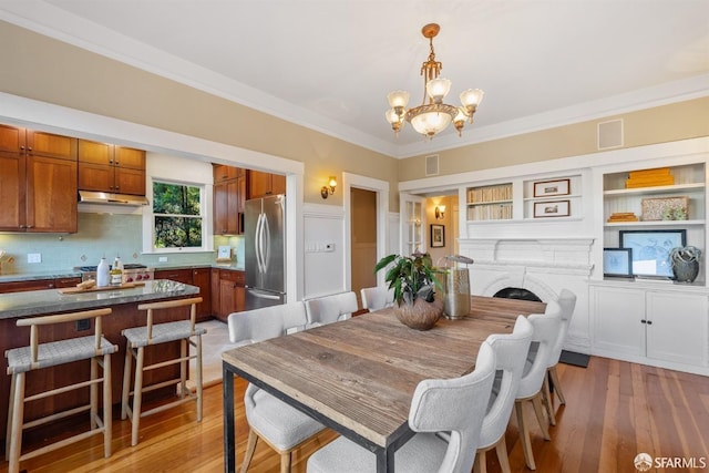 dining room featuring a notable chandelier, ornamental molding, a fireplace, and light wood-type flooring