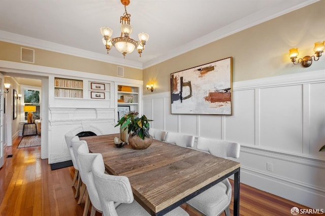 dining space with crown molding, wood-type flooring, a chandelier, and built in features