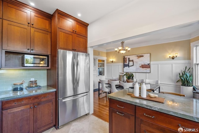 kitchen featuring pendant lighting, stainless steel refrigerator, tasteful backsplash, a notable chandelier, and light stone countertops