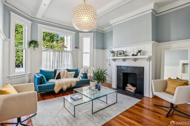 living room with wood-type flooring, a fireplace, ornamental molding, a notable chandelier, and beam ceiling