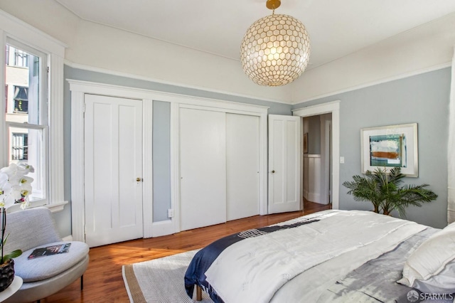 bedroom with hardwood / wood-style floors, a notable chandelier, and multiple closets