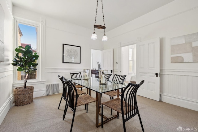 dining area with light carpet, a decorative wall, and wainscoting