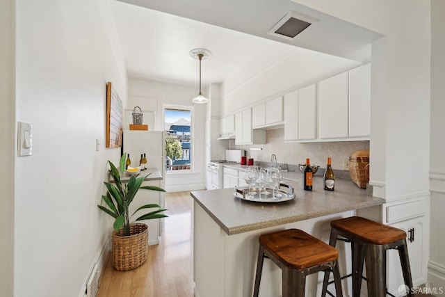 kitchen with white cabinets, a kitchen breakfast bar, backsplash, light wood-type flooring, and a peninsula