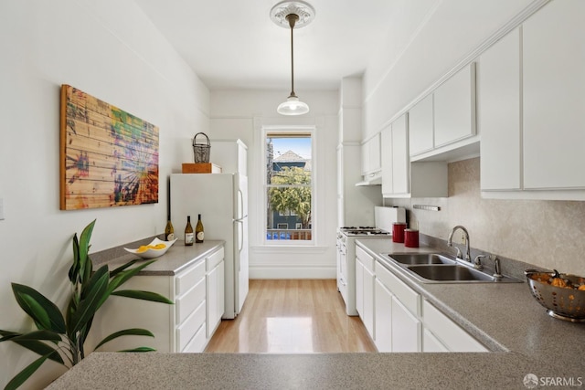 kitchen with a sink, white cabinets, white appliances, light wood-type flooring, and decorative light fixtures