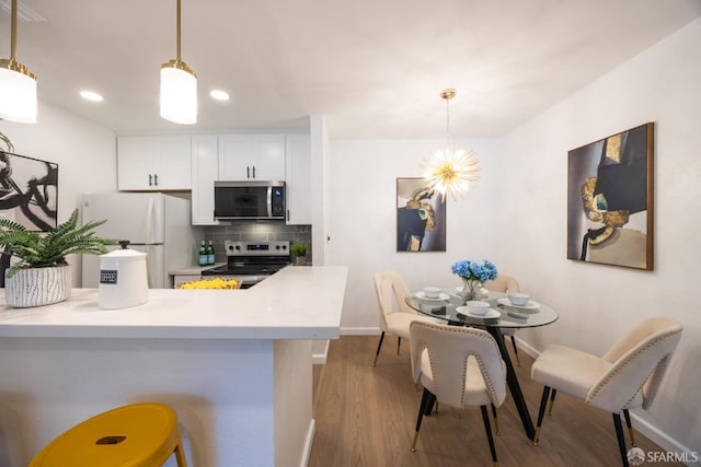 kitchen with white cabinetry, stainless steel appliances, decorative backsplash, decorative light fixtures, and kitchen peninsula