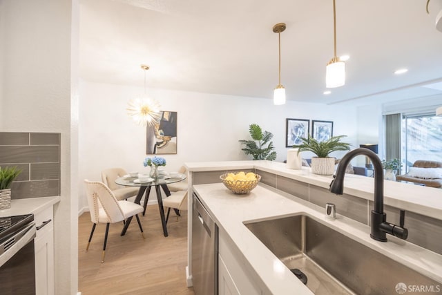 kitchen with sink, dishwasher, white cabinetry, hanging light fixtures, and light wood-type flooring