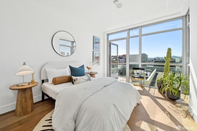 bedroom featuring a view of city, a wall of windows, wood finished floors, and baseboards