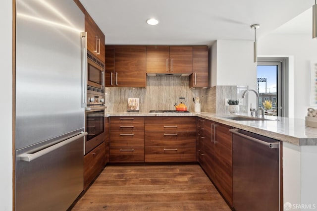 kitchen with built in appliances, a peninsula, a sink, and brown cabinets