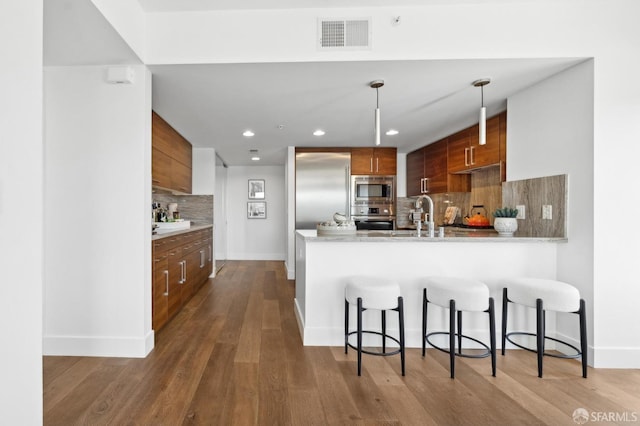 kitchen with a breakfast bar area, stainless steel appliances, a peninsula, visible vents, and brown cabinets