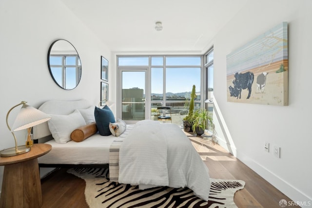 bedroom featuring access to outside, a wall of windows, wood finished floors, and baseboards