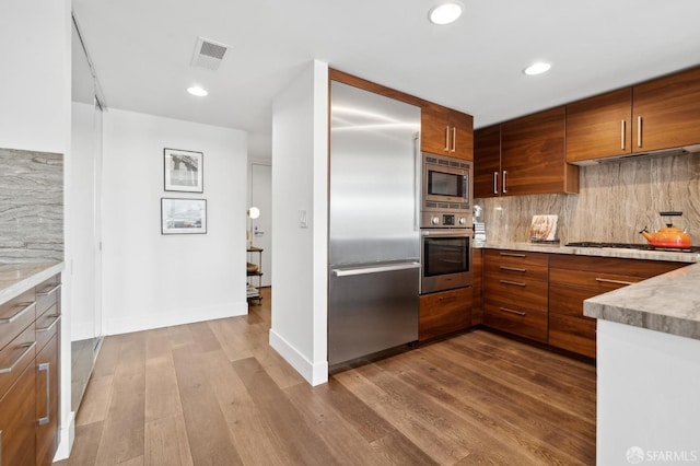 kitchen with tasteful backsplash, visible vents, dark wood finished floors, and built in appliances