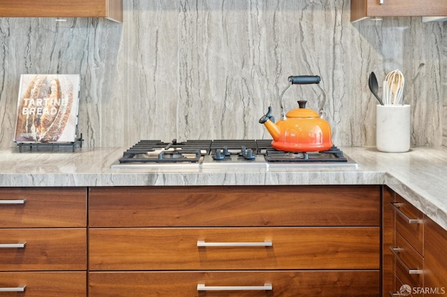 kitchen featuring brown cabinetry, stainless steel gas cooktop, light countertops, and backsplash