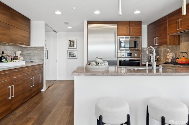 kitchen with built in appliances, a sink, dark wood-style floors, modern cabinets, and a kitchen bar