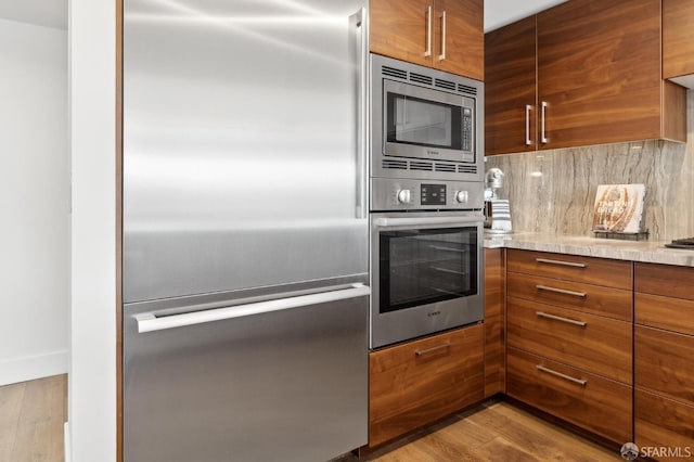 kitchen featuring built in appliances, wood finished floors, decorative backsplash, brown cabinetry, and modern cabinets