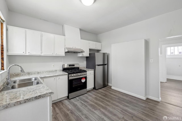kitchen with white cabinets, appliances with stainless steel finishes, a sink, wood finished floors, and under cabinet range hood