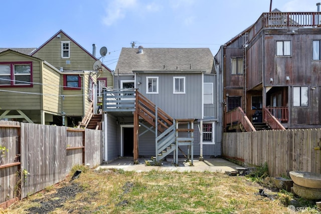 rear view of property with a fenced backyard, a wooden deck, a shingled roof, and stairway