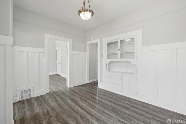 interior space featuring dark wood finished floors, visible vents, a wainscoted wall, and a decorative wall