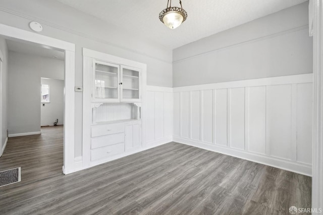 unfurnished room featuring a wainscoted wall, a decorative wall, dark wood finished floors, and visible vents