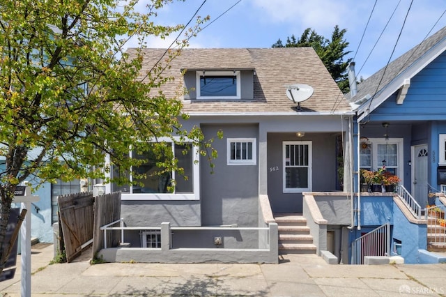 bungalow-style home featuring a porch, fence, roof with shingles, and stucco siding