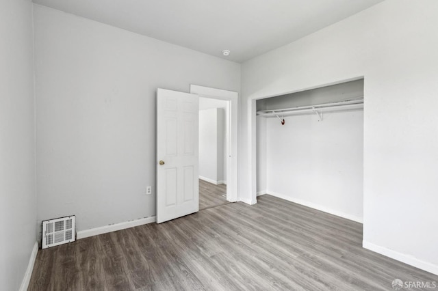 unfurnished bedroom with baseboards, visible vents, wood finished floors, and a closet